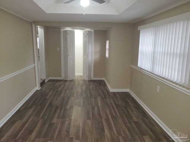 spare room featuring dark wood finished floors, baseboards, a tray ceiling, and a ceiling fan