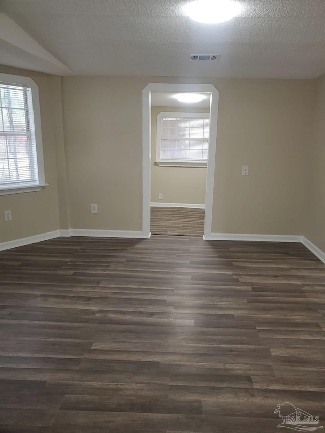 empty room with visible vents, a textured ceiling, baseboards, and dark wood-style flooring