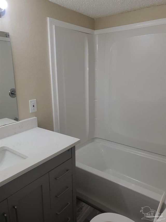 bathroom featuring toilet, a textured ceiling, vanity, and bathing tub / shower combination