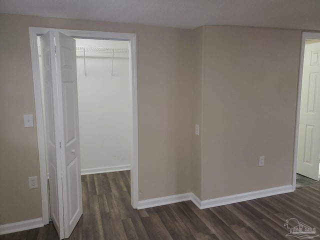 unfurnished bedroom with a walk in closet, dark wood-style floors, baseboards, and a closet