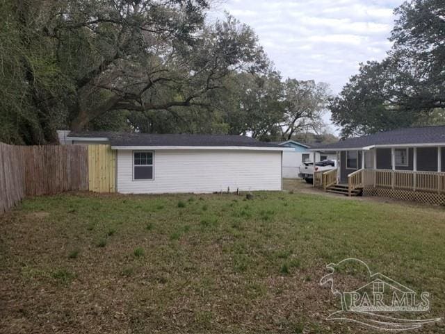 back of property with a yard, a wooden deck, and fence