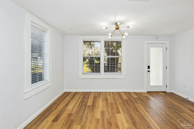 spare room with hardwood / wood-style floors and an inviting chandelier