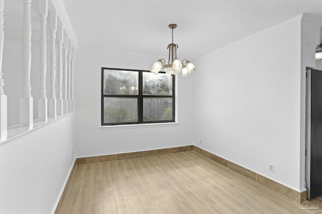 unfurnished dining area featuring a textured ceiling, ornamental molding, a chandelier, and light wood-type flooring