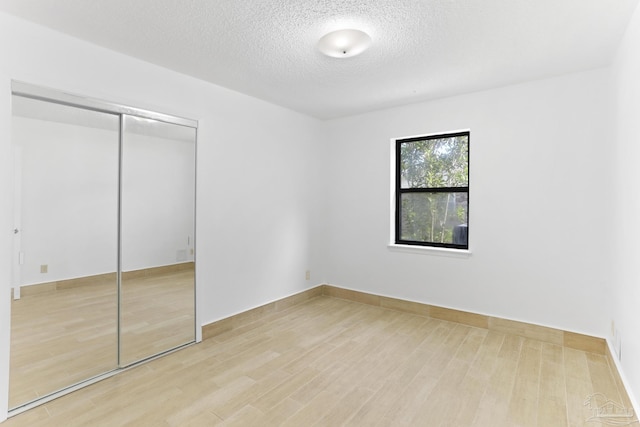 unfurnished bedroom with a textured ceiling, light wood-type flooring, and a closet