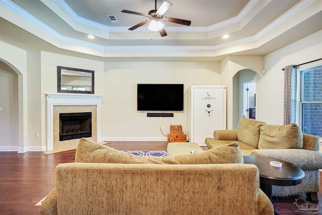 living room featuring ceiling fan, ornamental molding, a tray ceiling, a fireplace, and dark hardwood / wood-style flooring