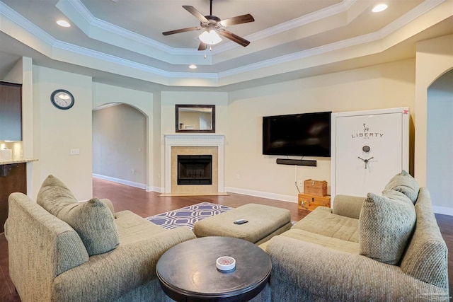 living room featuring a tray ceiling, dark wood-type flooring, a fireplace, and crown molding