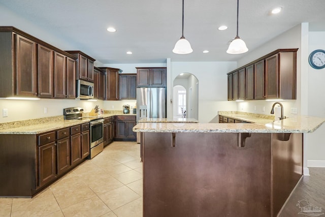 kitchen featuring light stone counters, hanging light fixtures, kitchen peninsula, appliances with stainless steel finishes, and a breakfast bar