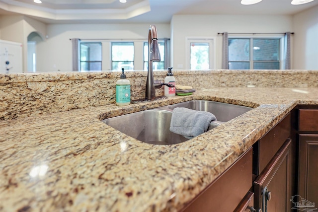 kitchen featuring light stone counters, a raised ceiling, plenty of natural light, and sink