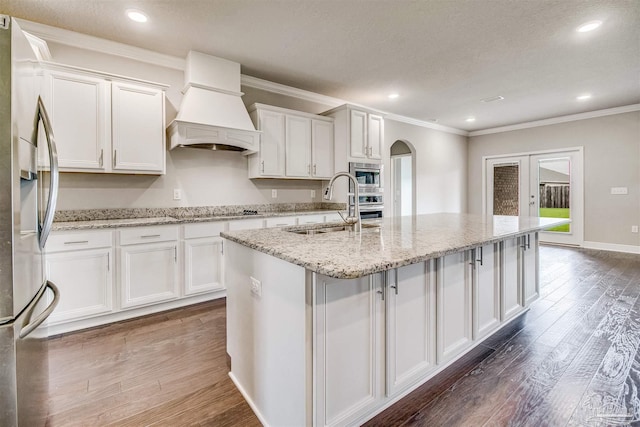 kitchen with white cabinetry, sink, custom range hood, and a center island with sink