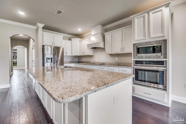 kitchen with white cabinetry, stainless steel appliances, custom range hood, and a center island with sink