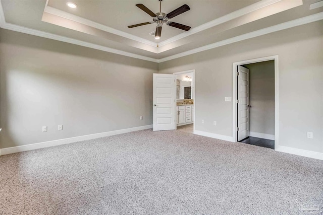 unfurnished bedroom with ensuite bathroom, a walk in closet, a tray ceiling, ceiling fan, and carpet