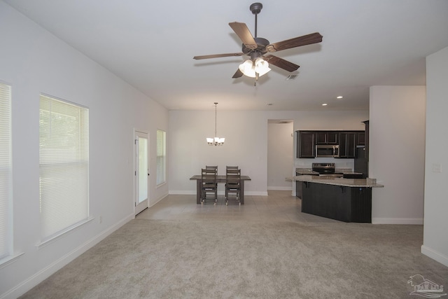 interior space with pendant lighting, light colored carpet, a breakfast bar area, ceiling fan with notable chandelier, and appliances with stainless steel finishes