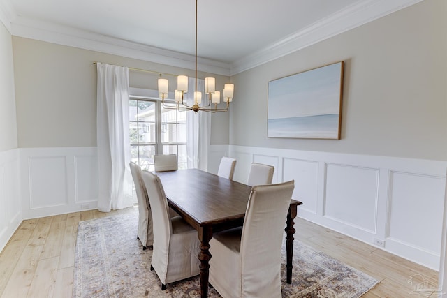 dining space with crown molding, wainscoting, light wood-type flooring, a notable chandelier, and a decorative wall