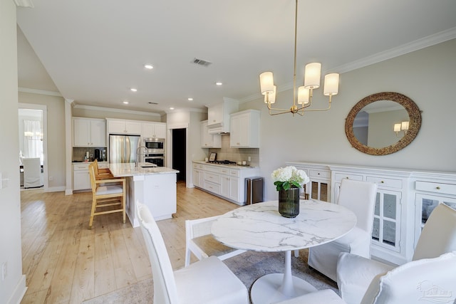 dining room featuring ornamental molding, a notable chandelier, light wood finished floors, and visible vents