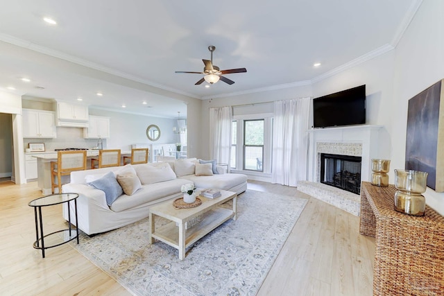 living area featuring crown molding, light wood-style floors, ceiling fan, and a fireplace