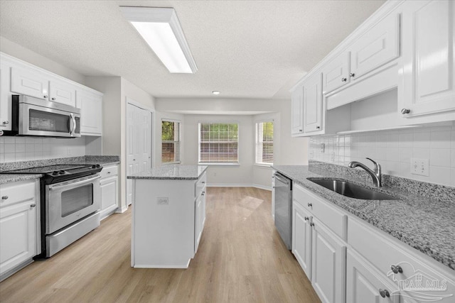 kitchen with light wood finished floors, white cabinets, a sink, and appliances with stainless steel finishes