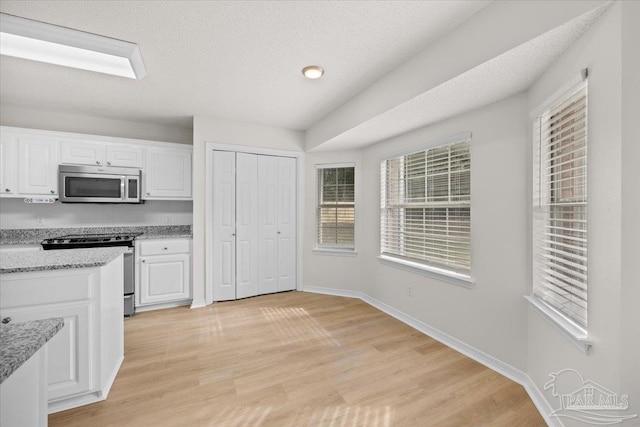 kitchen with light wood finished floors, light stone countertops, appliances with stainless steel finishes, and white cabinetry