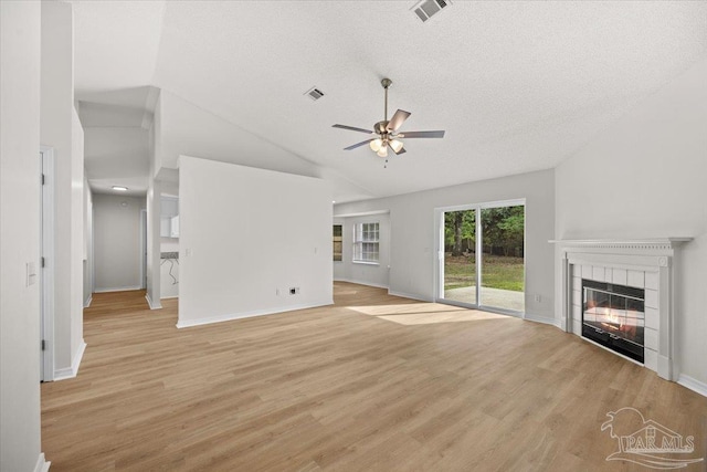 unfurnished living room featuring lofted ceiling, light wood finished floors, visible vents, a tiled fireplace, and ceiling fan