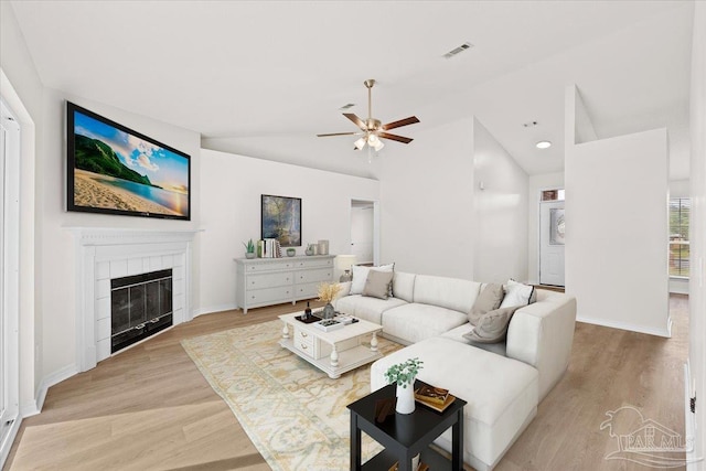 living area with vaulted ceiling, a ceiling fan, light wood-style flooring, a tiled fireplace, and visible vents
