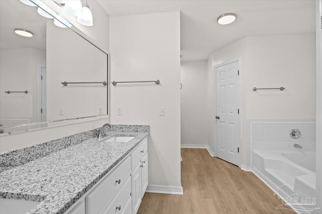 bathroom with baseboards, a garden tub, wood finished floors, and vanity