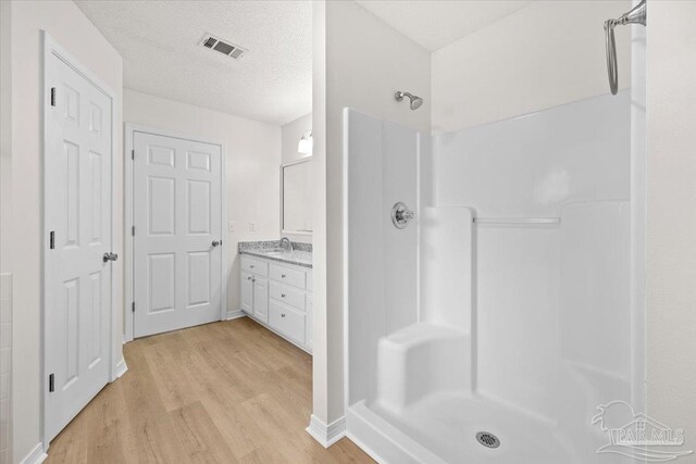 full bath with vanity, wood finished floors, visible vents, and a shower
