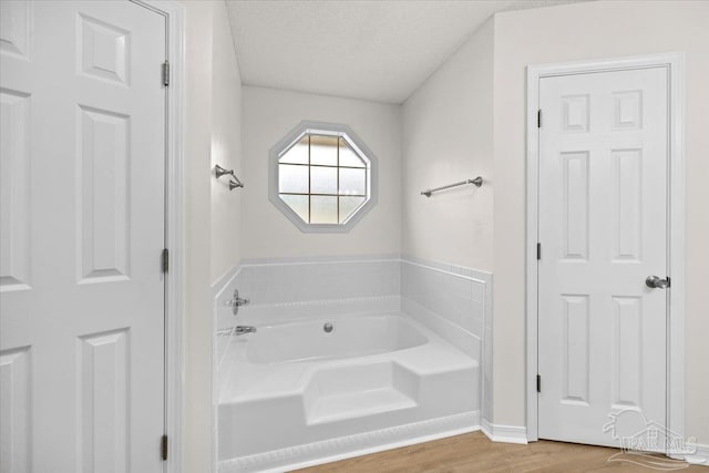 full bathroom with a bath, baseboards, wood finished floors, and a textured ceiling