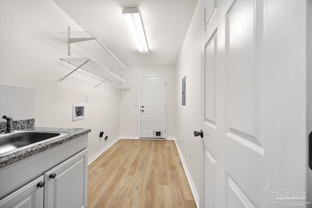 clothes washing area with a sink, electric panel, cabinet space, light wood finished floors, and washer hookup