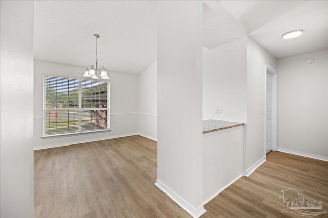 unfurnished dining area featuring wood finished floors, baseboards, and an inviting chandelier