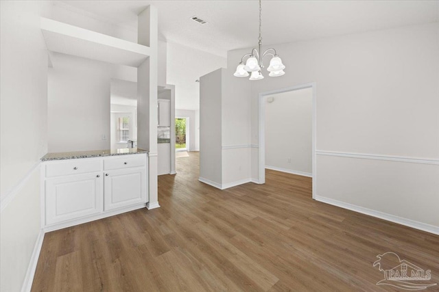 unfurnished dining area with baseboards, visible vents, an inviting chandelier, wood finished floors, and high vaulted ceiling