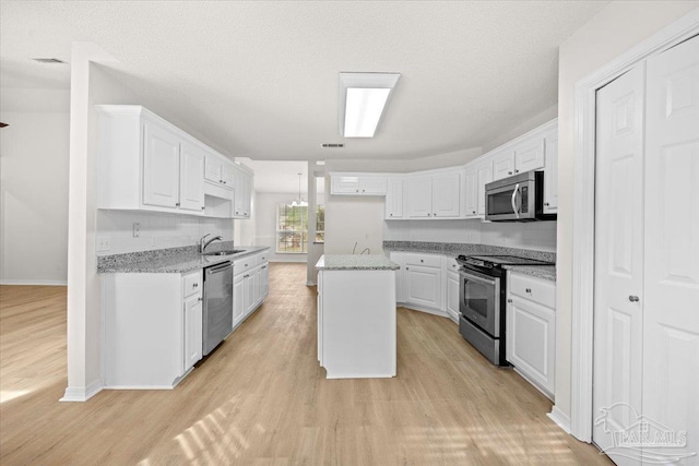 kitchen with a sink, stainless steel appliances, light wood finished floors, baseboards, and white cabinetry