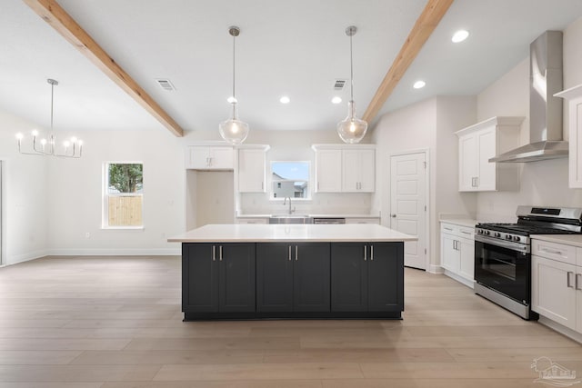 kitchen featuring hanging light fixtures, a center island, wall chimney range hood, and stainless steel gas range