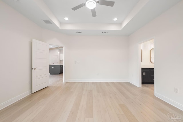 empty room featuring a raised ceiling, ceiling fan, and light wood-type flooring