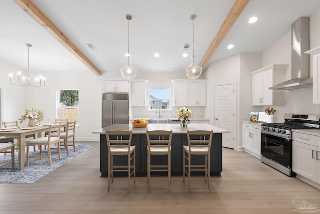 kitchen with wall chimney range hood, hanging light fixtures, stainless steel appliances, white cabinets, and a kitchen island