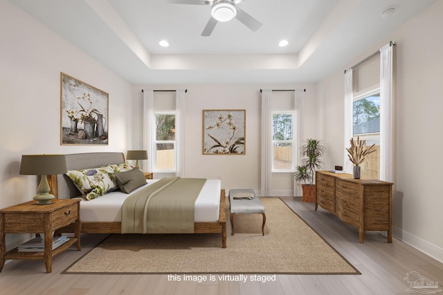 bedroom featuring light hardwood / wood-style flooring, ceiling fan, and a tray ceiling