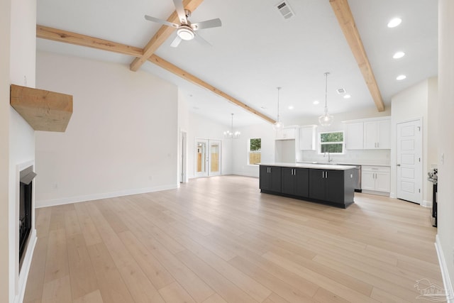 unfurnished living room with white cabinetry, sink, hanging light fixtures, a center island, and light hardwood / wood-style flooring