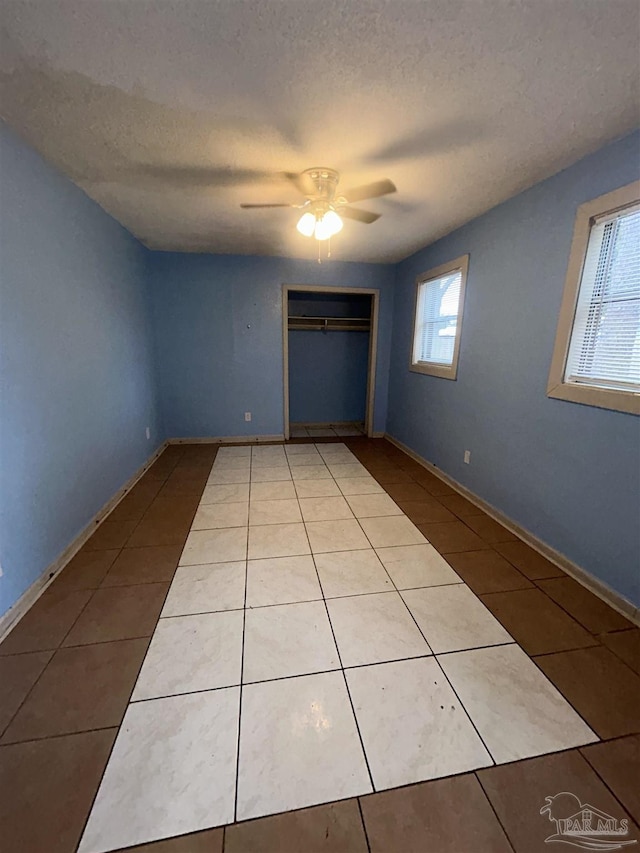 unfurnished bedroom with multiple windows, ceiling fan, light tile patterned flooring, and a textured ceiling