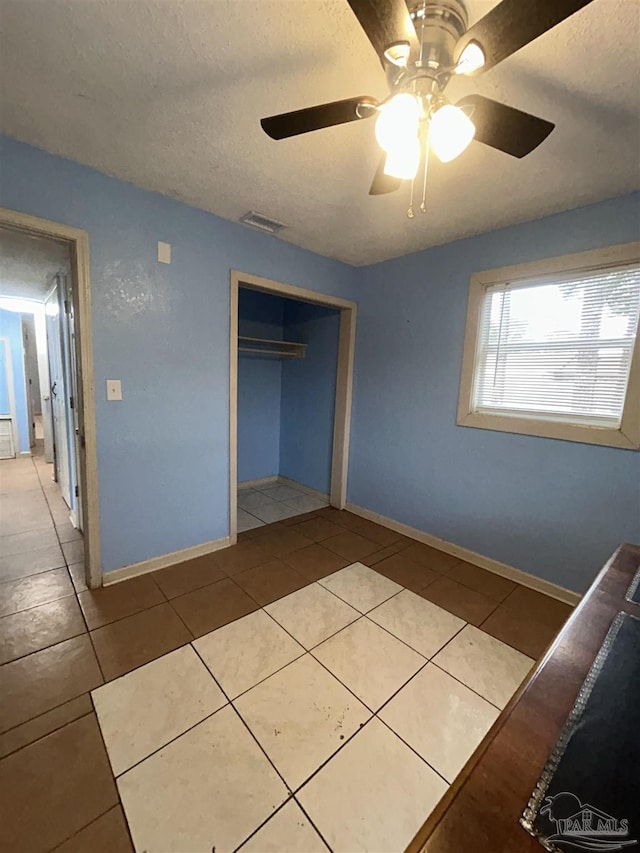 unfurnished bedroom featuring ceiling fan, light tile patterned floors, and a textured ceiling