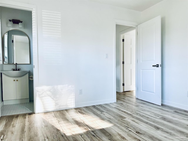 unfurnished bedroom with arched walkways, wood finished floors, baseboards, and a sink