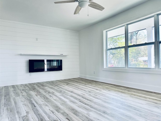 unfurnished living room featuring wooden walls, wood finished floors, baseboards, and ceiling fan