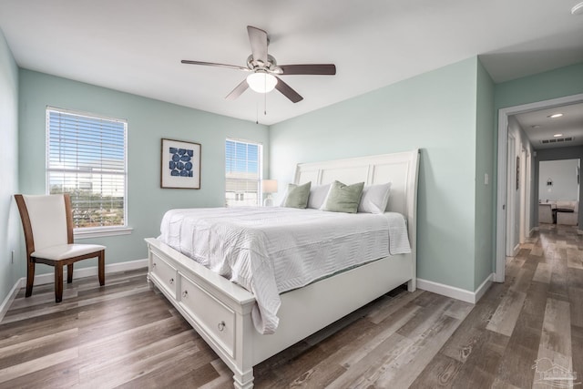 bedroom with a ceiling fan, visible vents, baseboards, and wood finished floors