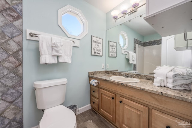 bathroom featuring baseboards, toilet, wood finished floors, walk in shower, and vanity