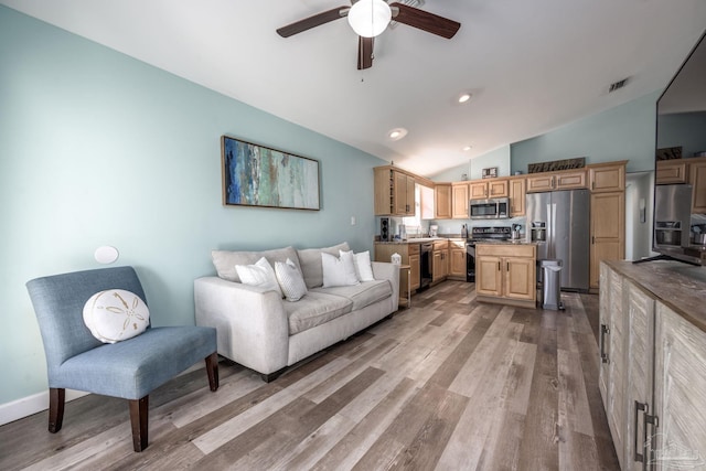 living area with visible vents, baseboards, ceiling fan, light wood-style flooring, and vaulted ceiling