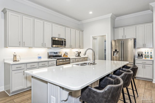 kitchen with a breakfast bar area, crown molding, a sink, stainless steel appliances, and light wood-style flooring