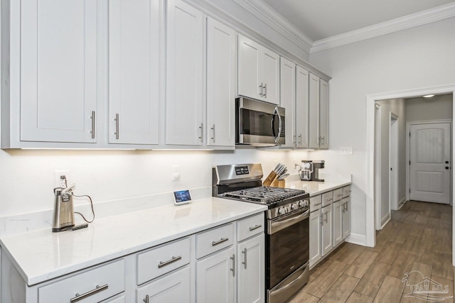 kitchen featuring crown molding, baseboards, light wood-type flooring, light stone counters, and appliances with stainless steel finishes
