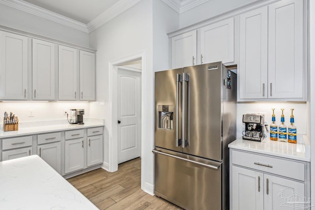 kitchen featuring light stone counters, light wood-style floors, baseboards, ornamental molding, and high quality fridge