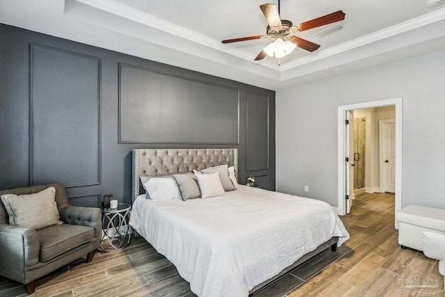 bedroom with a tray ceiling, ceiling fan, ornamental molding, and wood finished floors