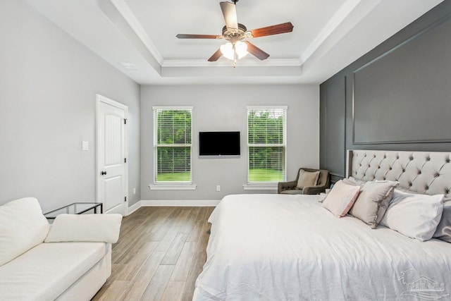 bedroom featuring ceiling fan, wood finished floors, baseboards, ornamental molding, and a tray ceiling