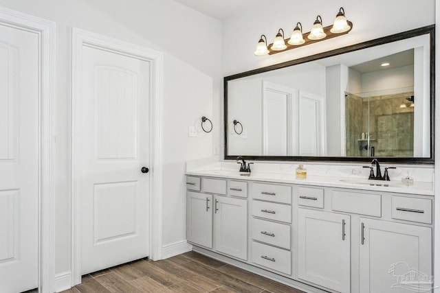full bathroom with wood finished floors, double vanity, a sink, and a stall shower