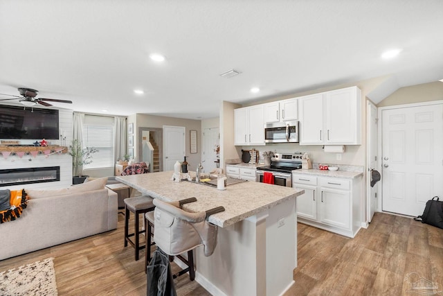 kitchen with light wood-style flooring, a breakfast bar area, appliances with stainless steel finishes, open floor plan, and a sink