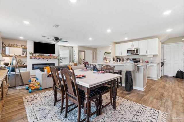 dining area featuring ceiling fan, light hardwood / wood-style flooring, brick wall, and a large fireplace